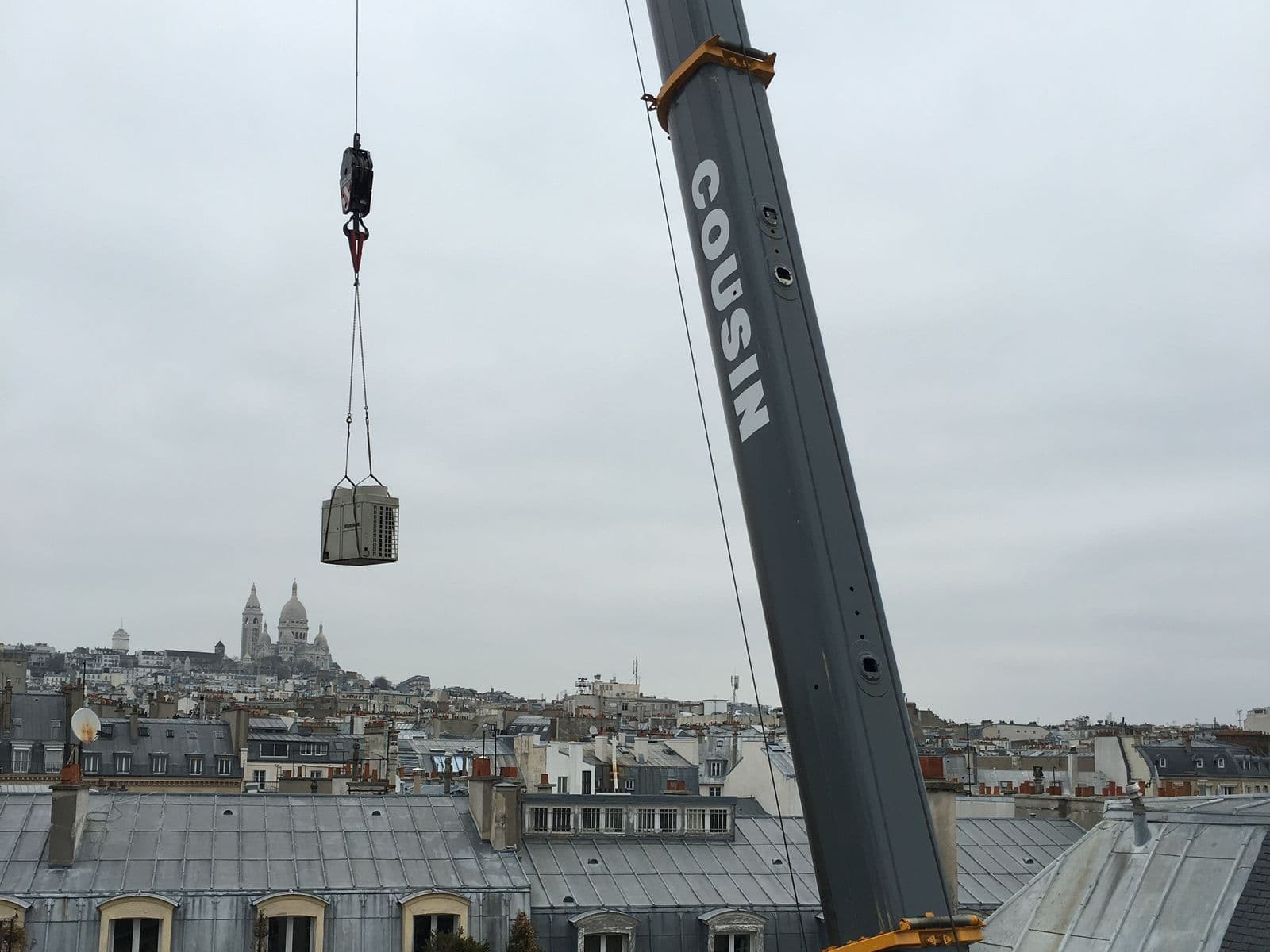 Groupe de climatisation hissé par une grue au-dessus des toits de Paris